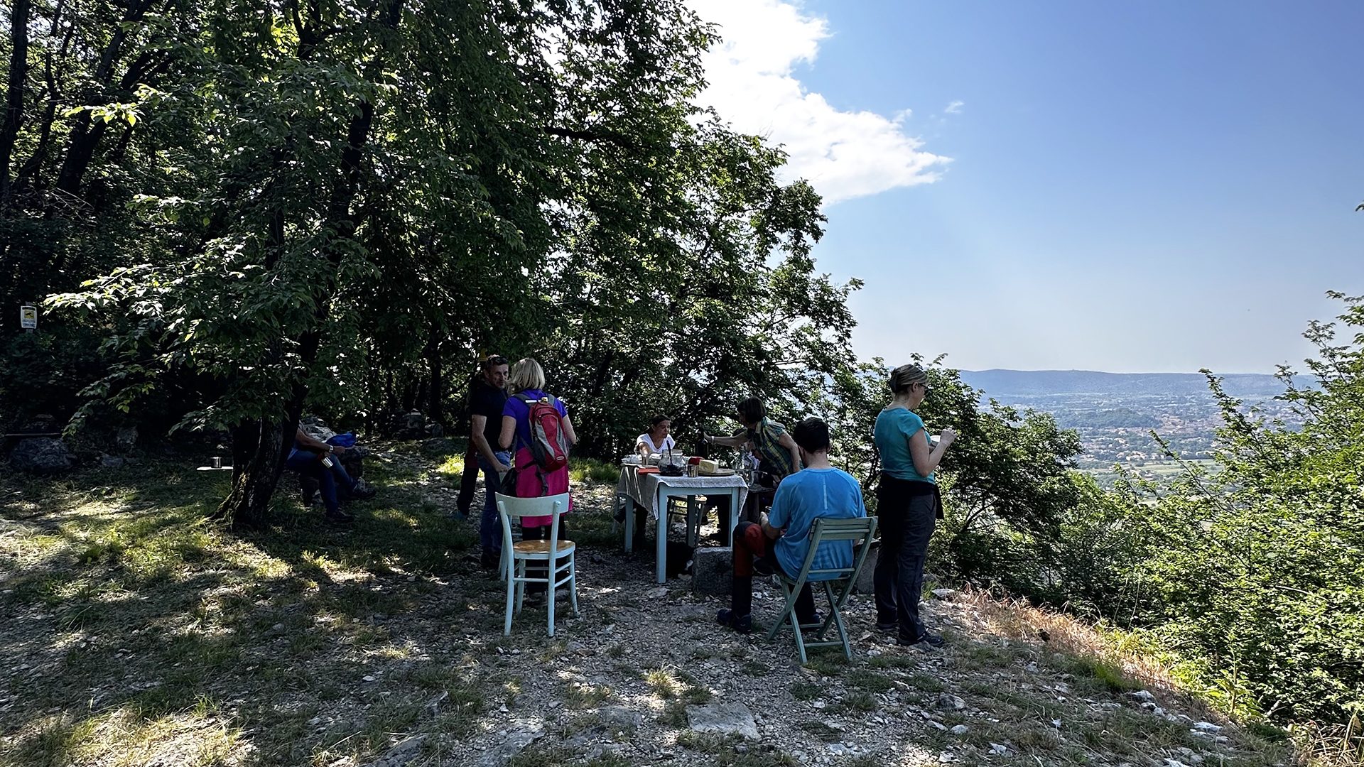 Escursionisti seduti ai tavoli nel bosco, con la vista sulla pianura