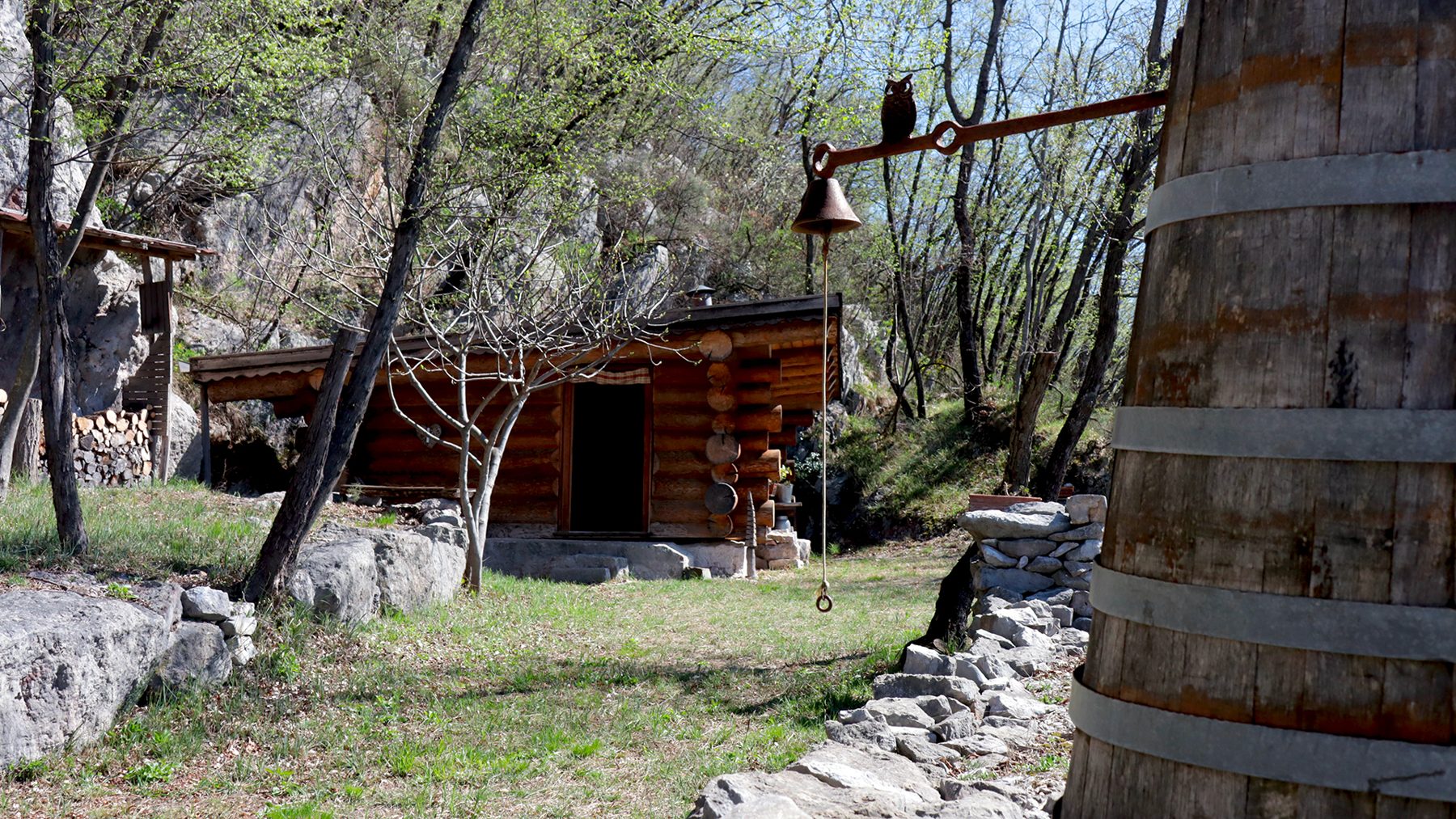La Blockhouse di legno tra gli alberi del Sabotino, con una botte in primo piano e la campana appesa a un ramo
