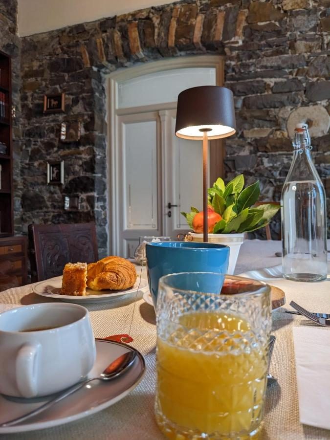 La colazione servita in sala: caffè, spremuta d’arancia e cornetti sul tavolo, davanti alla parete in pietra