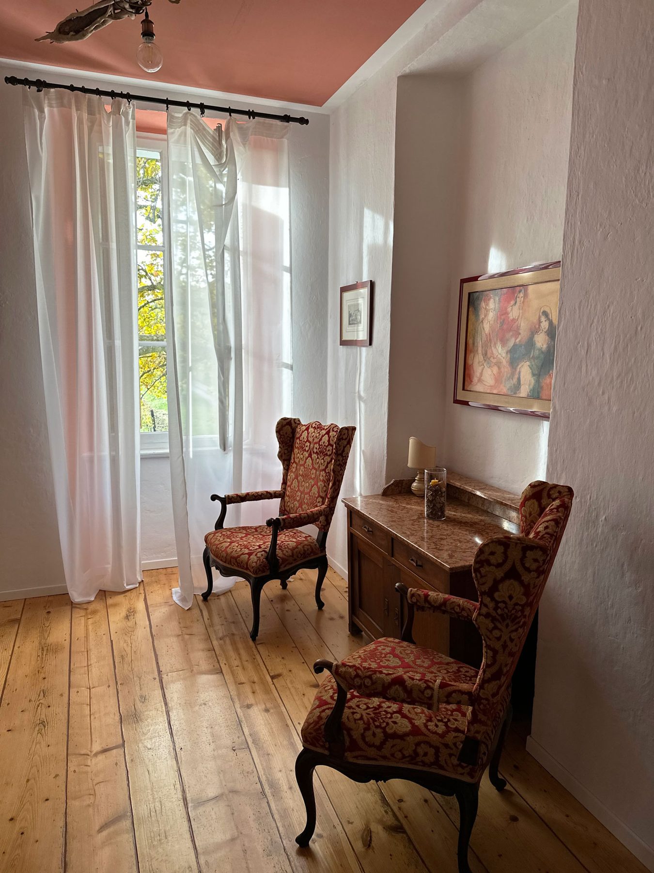 Una camera della villa con la luce che entra dalla finestra, le tende leggere e due poltrone d’epoca