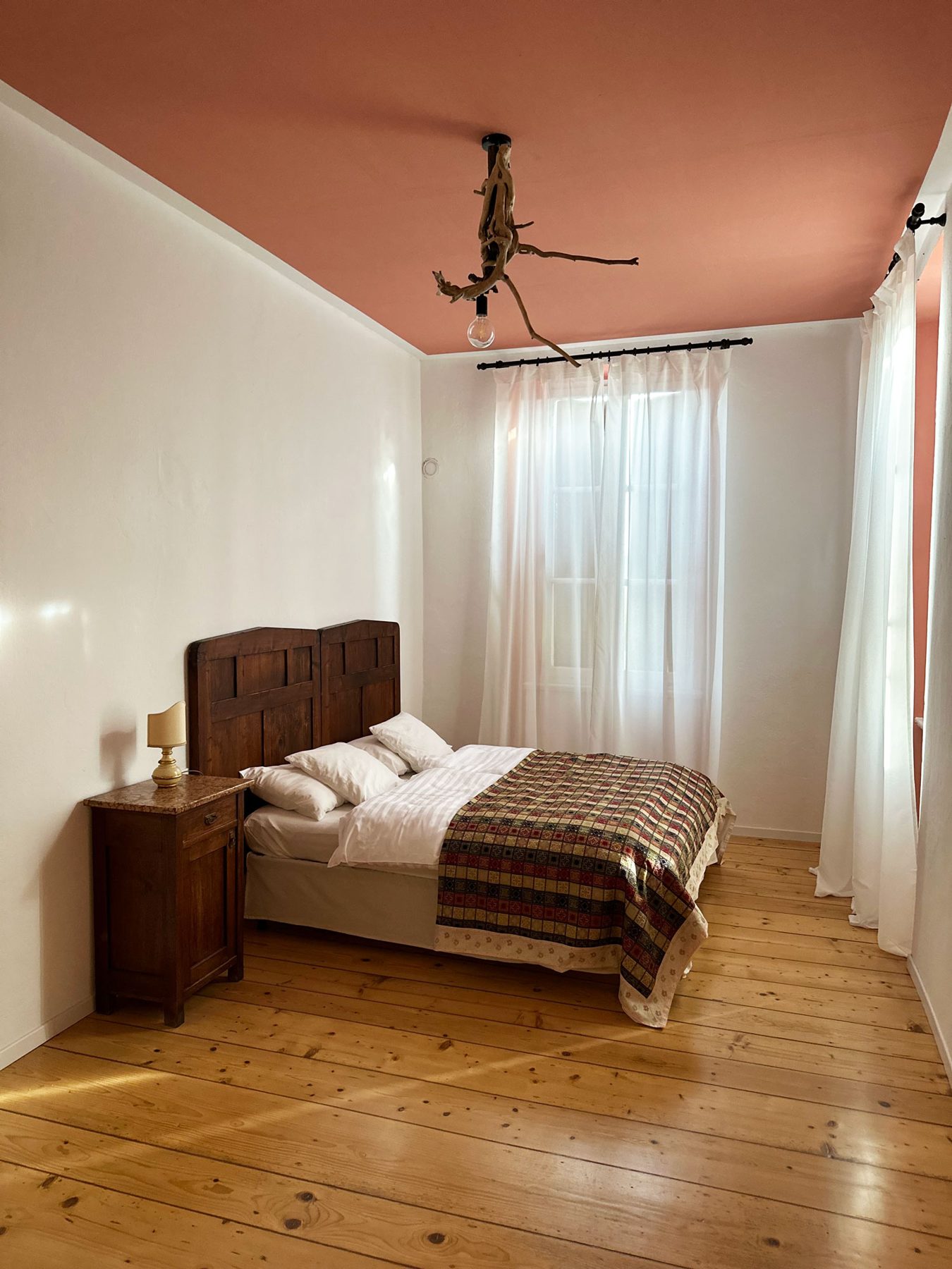 Una camera dal soffitto rosa, con il letto in legno antico e il pavimento in tavole di abete