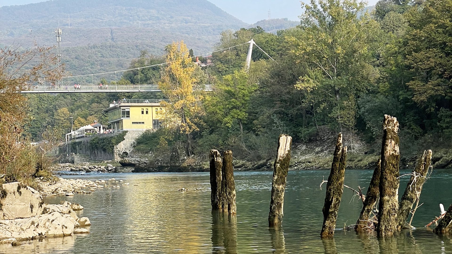 I resti in legno di un antico ponte nell’acqua dell’Isonzo, con una passerella sullo sfondo